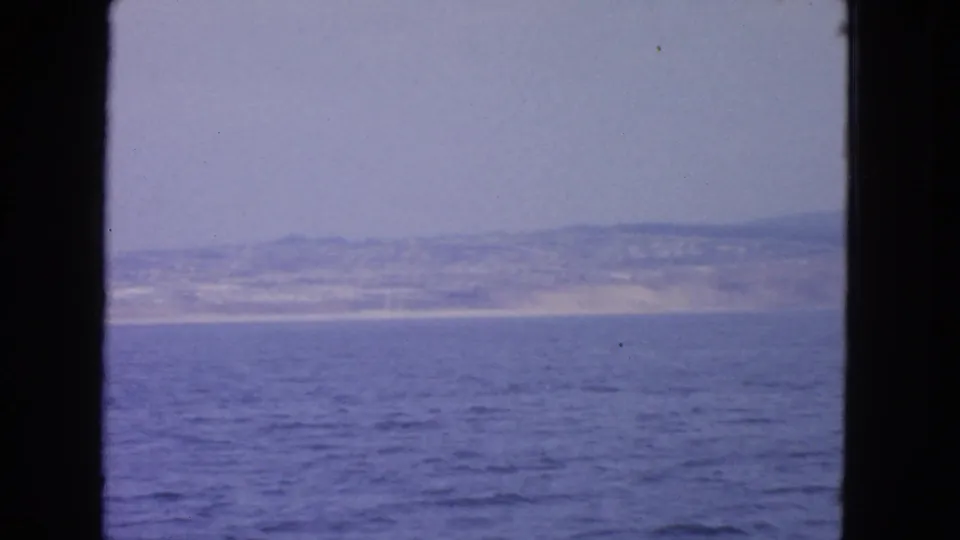 1963 San Francisco Bay-area frame showing open water and a distant coast with hills, seen through dark boat-window edges.