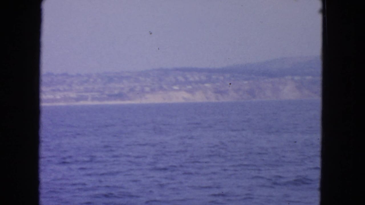 Blue water seen through dark frame edges toward a hazy distant shoreline and hills.