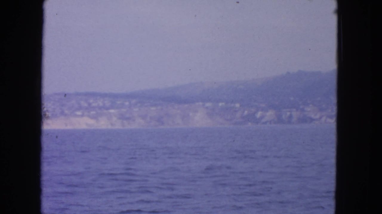 Distant coastline and hillside beyond blue water, bordered by dark vertical frame edges.