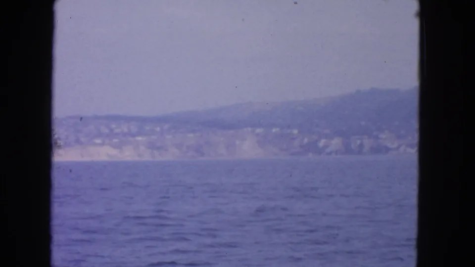San Francisco-area coastline in 1963 home-movie footage, with calm blue water, hazy hills, and shoreline buildings seen from a vessel.
