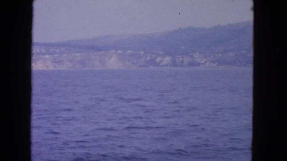 A 1963 8mm vessel view toward the San Francisco-area coast, showing open blue water, distant pale cliffs, and soft hillside development.