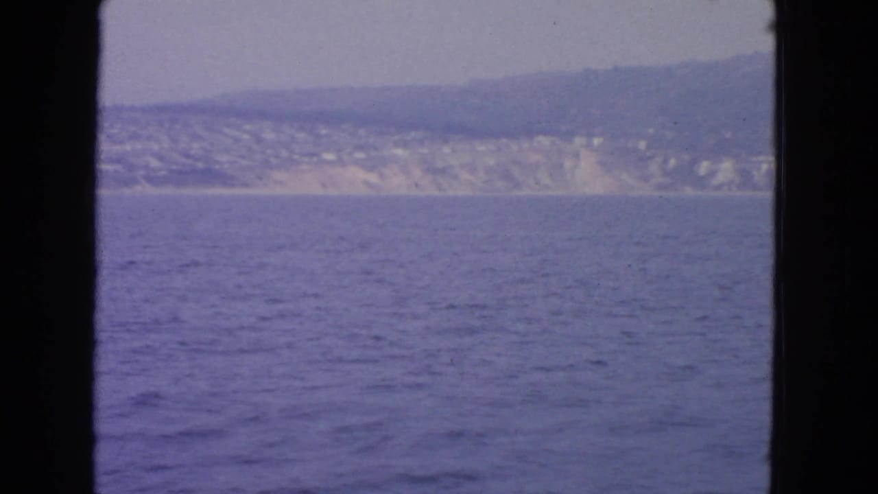 Distant hazy coastline beyond blue water, framed by dark film borders.