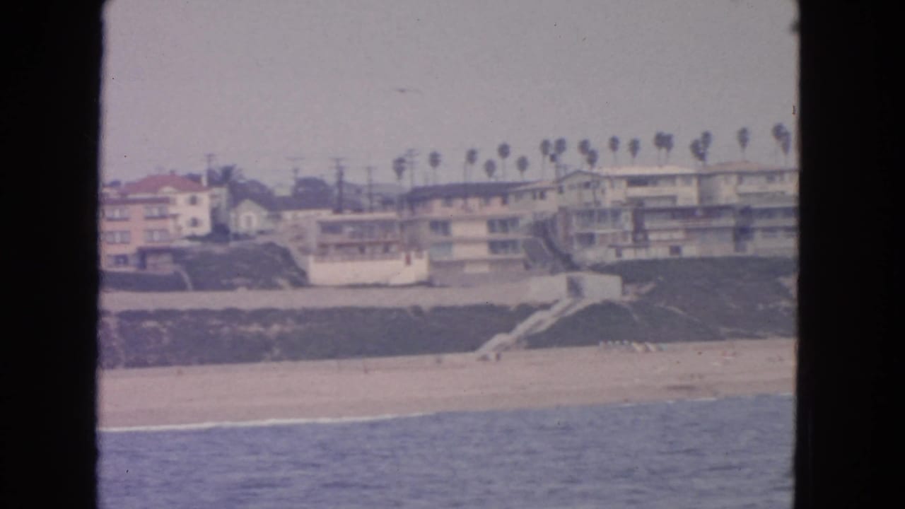 Coastal buildings and palm trees above a sandy beach, seen from the water.