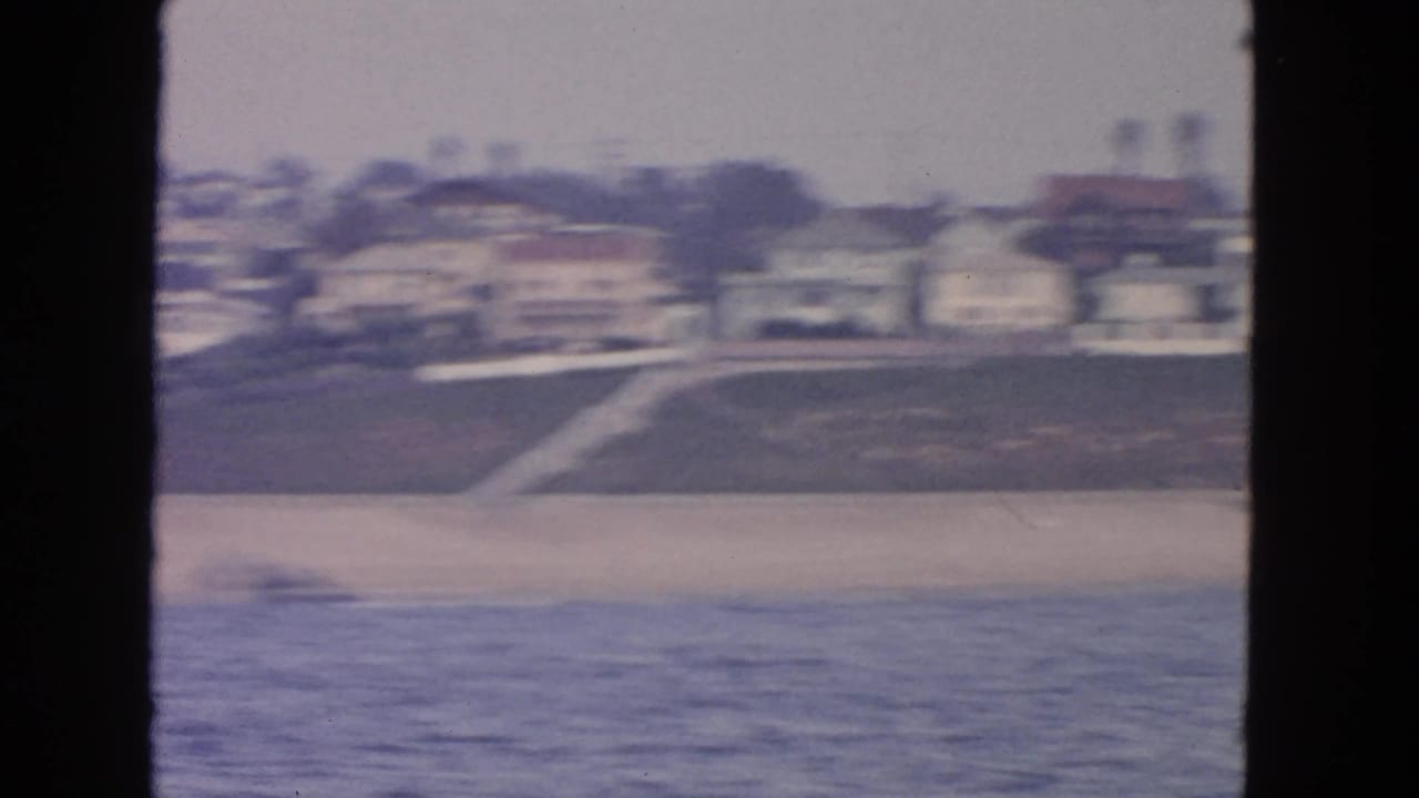 Beach shoreline with ocean foreground, hillside homes, and a sloped access path.