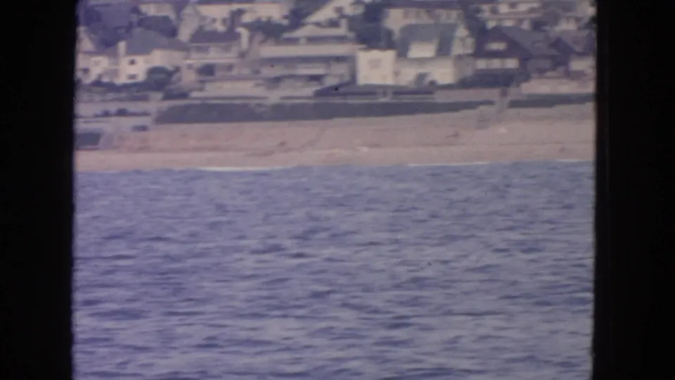 1963 San Francisco coastal view from offshore, with water, empty sand, and houses lining the beach edge.