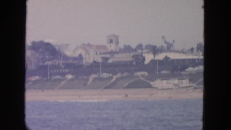 Distant San Francisco shoreline frame with beach, homes, trees, and a small boat-like shape near the waterline.