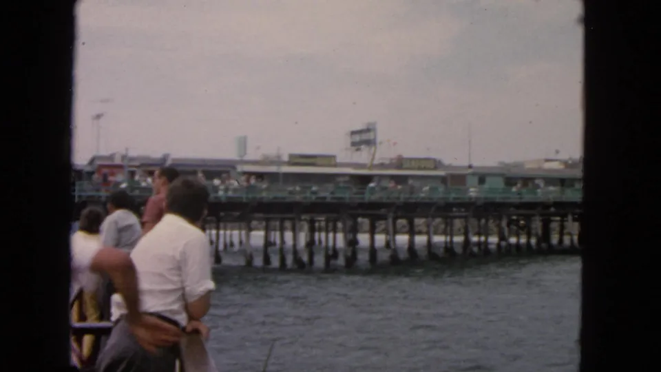 1963 San Francisco waterfront seen from a boat, with passengers in period clothing facing a pier.