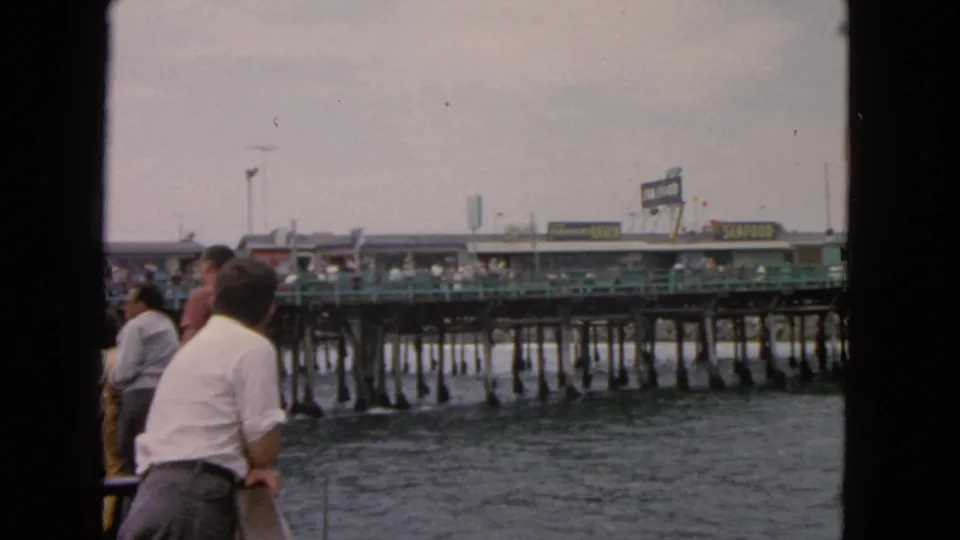 1963 San Francisco home-movie frame showing a man at the boat rail with the pier and water beyond.