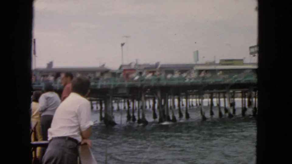 1963 San Francisco boat footage with passengers watching a long waterfront pier under a gray sky.