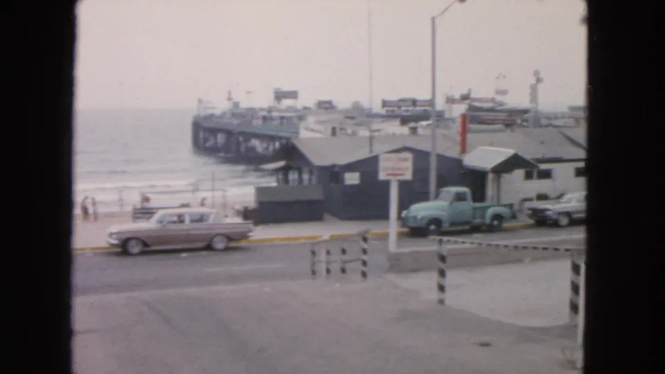 A wider 1963 San Francisco waterfront view shows parked mid-century cars, a light blue pickup, small beach buildings, the ocean, and a long pier.