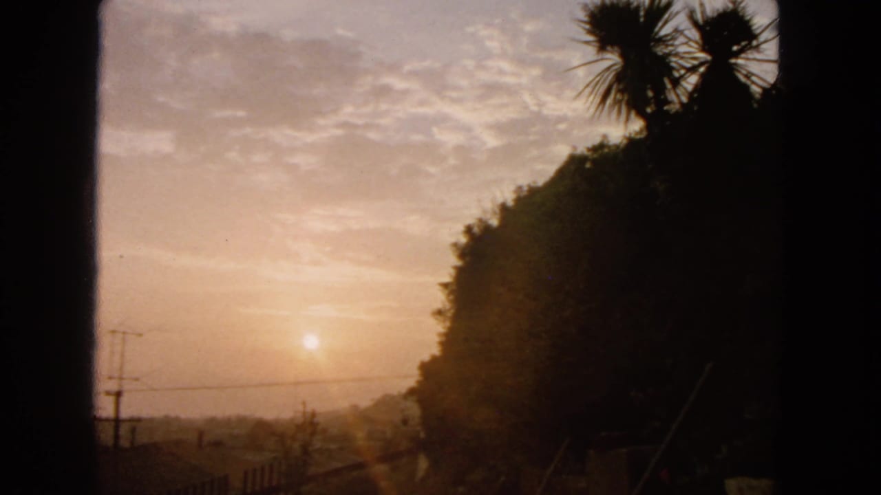 1963 8mm San Francisco hillside view with a hazy sun, clouded sky, dark vegetation, utility poles, and overhead wires.