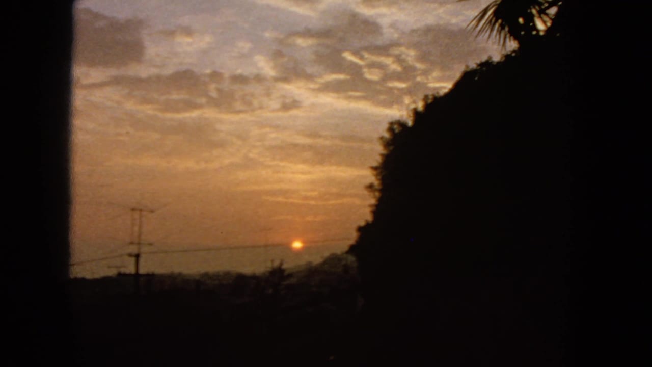 1963 San Francisco 8mm frame with the sunset lower in the sky, dark hillside massing, utility pole silhouettes, and warm cloud cover.