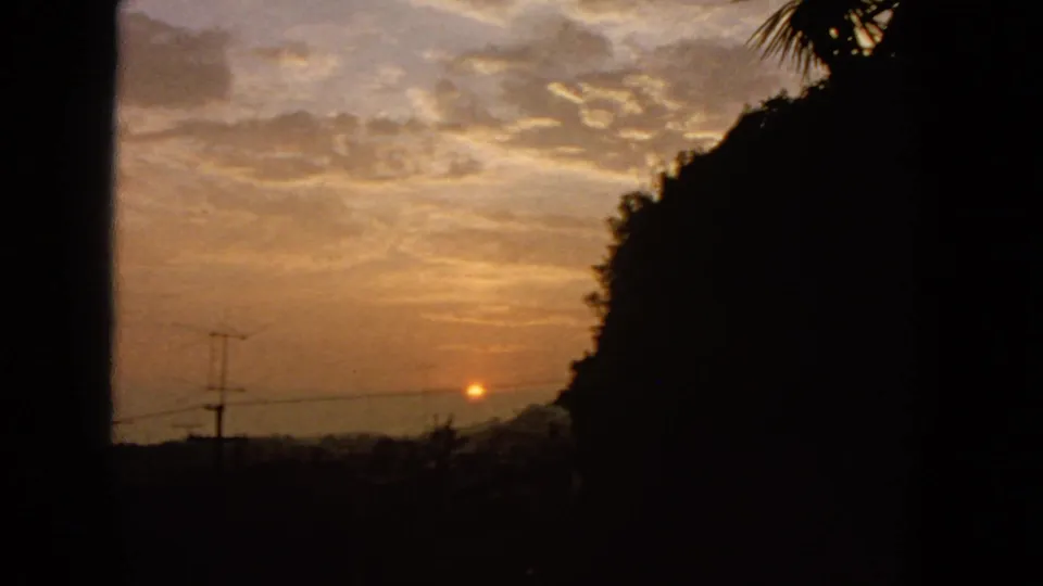 1963 San Francisco 8mm frame with the sunset lower in the sky, dark hillside massing, utility pole silhouettes, and warm cloud cover.