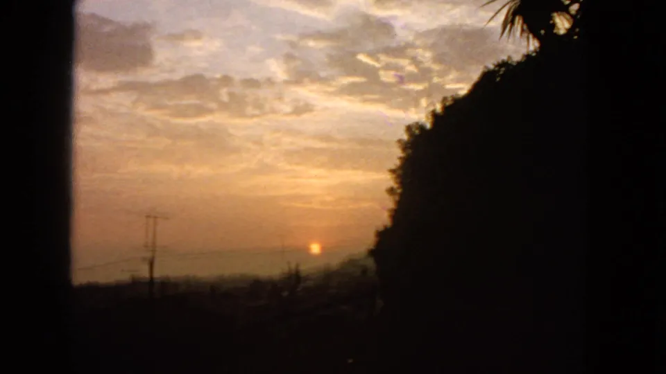 1963 San Francisco 8mm frame showing a brighter cloud field, small orange sun, silhouetted utility pole, and darkened hillside edge.