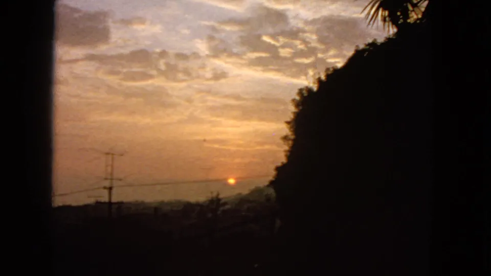 1963 San Francisco 8mm frame with a low orange sun, layered clouds, silhouetted hillside, utility pole, wires, and visible film-frame borders.