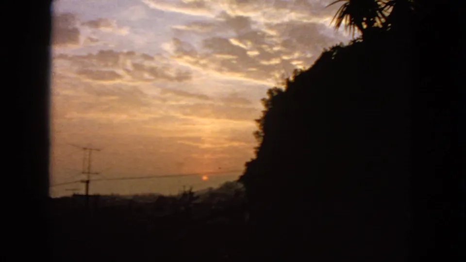 1963 San Francisco frame showing a fading orange sun, layered clouds, dark shaded foreground, utility lines, and a hillside silhouette.