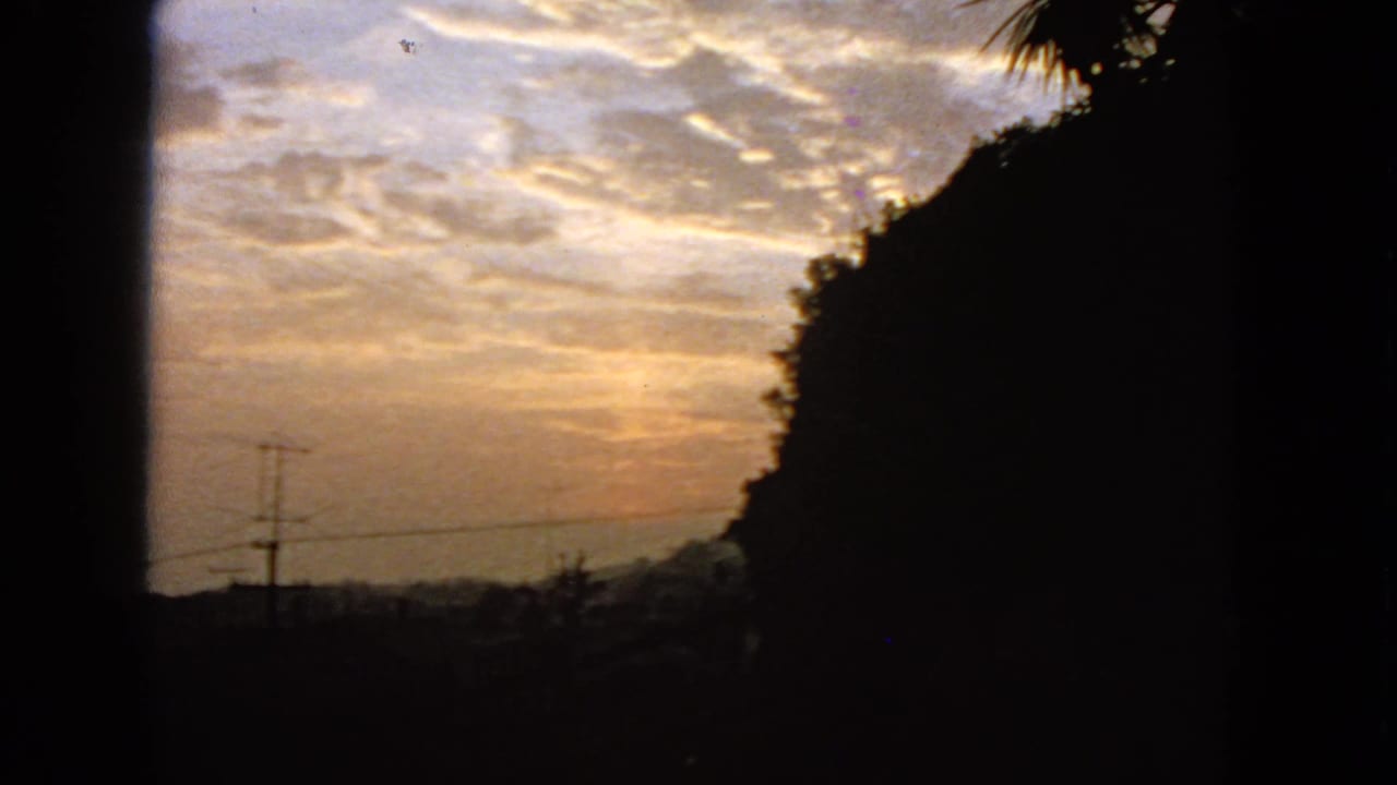 1963 San Francisco frame with mottled sunset clouds, a silhouetted slope, palm-like foliage, and faint utility lines.