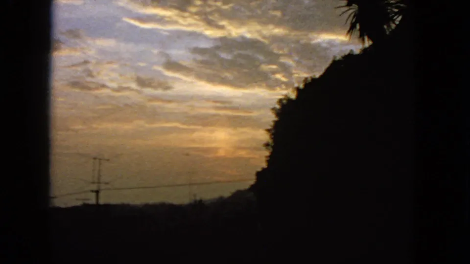 1963 San Francisco 8mm frame showing golden cloud bands, silhouetted vegetation, utility lines, and dark frame edges.