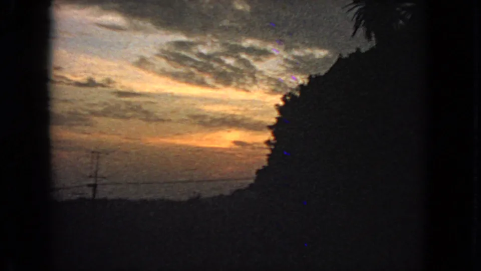 Later 1963 San Francisco sunset frame with deeper shadows, orange horizon light, a utility pole, wires, and heavy 8mm grain.