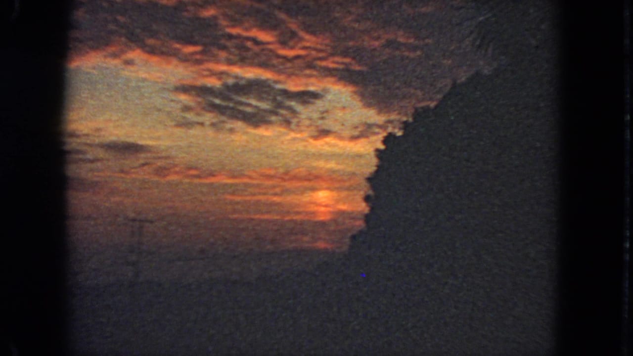 1963 San Francisco 8mm frame showing a glowing sunset sky behind a dark urban or hillside silhouette.