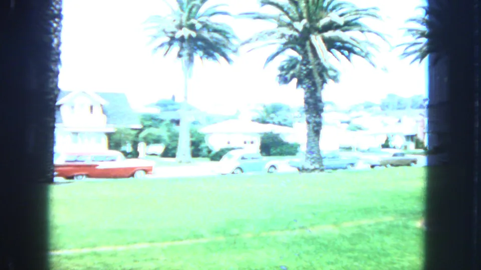 1963 San Francisco 8mm frame showing a bright palm-lined residential street with grass, houses, and parked cars.