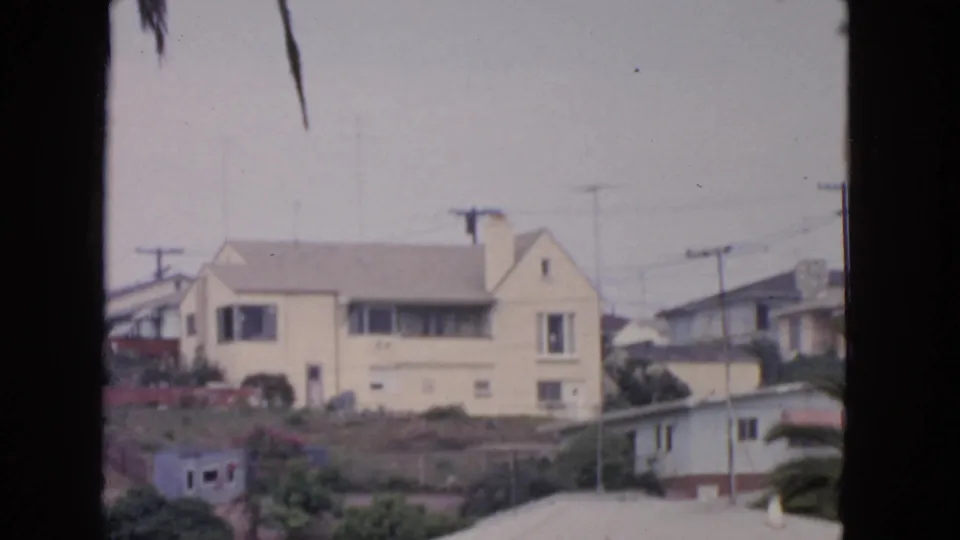 A cream-colored San Francisco hillside house with TV antennas and nearby utility poles appears in soft 1963 8mm color.