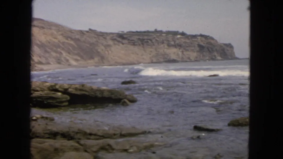 1963 San Francisco coastal view on 8mm film, showing surf rolling toward rocks below pale cliffs and dark foreground framing.