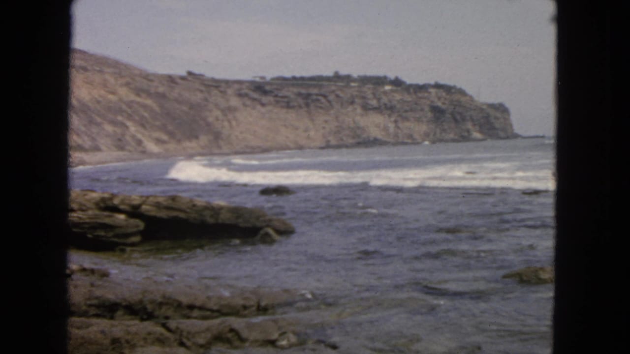 Ocean waves roll across a rocky shore with cliffs in the background.