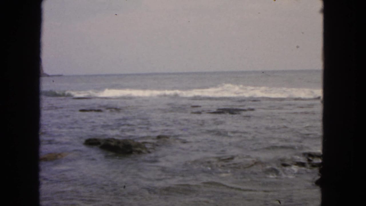 1963 San Francisco shoreline footage showing low surf, scattered rocks, and a pale horizon through a dark foreground frame.