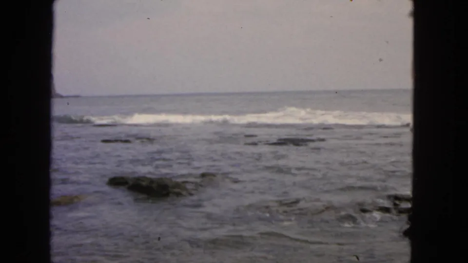 1963 San Francisco shoreline footage showing low surf, scattered rocks, and a pale horizon through a dark foreground frame.
