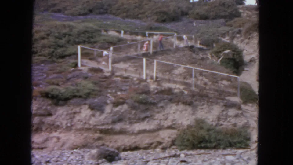 1963 San Francisco 8mm frame with distant people near white railings on a rugged outdoor hillside path.