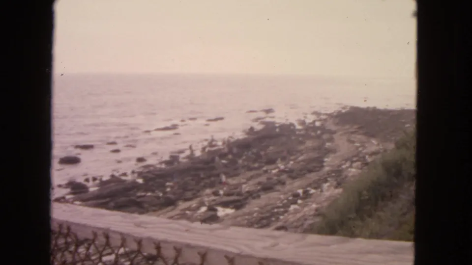 1963 San Francisco-area shoreline view with a road above tide pools and small distant figures on the rocky beach.