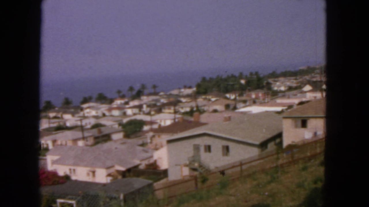 Elevated 1963 view of coastal residential buildings near San Francisco, framed by 8mm gate edges and a hazy ocean backdrop.