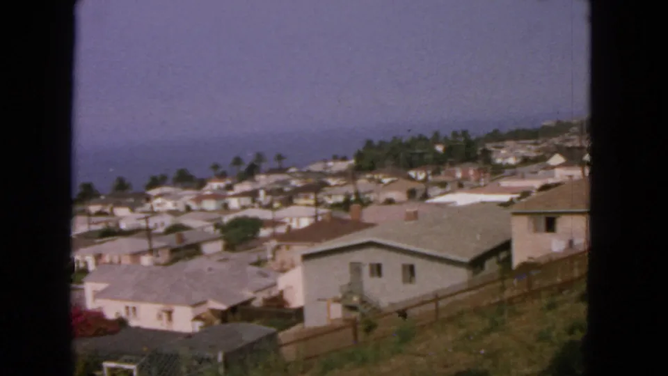 Elevated 1963 view of coastal residential buildings near San Francisco, framed by 8mm gate edges and a hazy ocean backdrop.