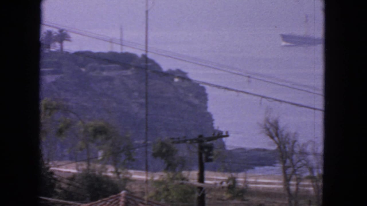 Rocky coastal bluff with utility lines and a distant ship on hazy water.