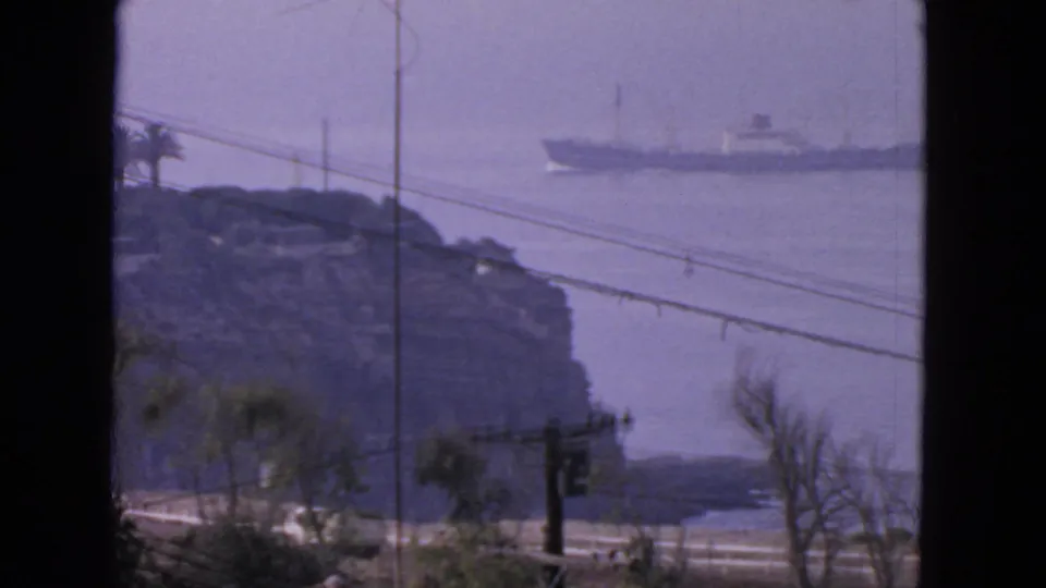 1963 San Francisco shoreline view showing a ship on the bay behind a rocky point, with road, wires, utility pole, and trees below.