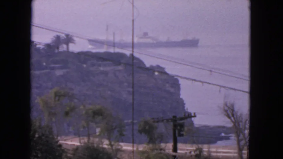 The 8mm frame holds on a distant liner near San Francisco, with a rocky island, palms, wires, and purple haze visible.