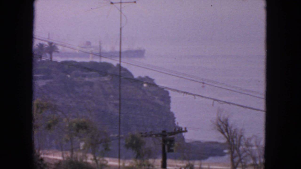 1963 San Francisco coastal home-movie frame with offshore ship, hazy water, bluff, utility pole, and foreground lines.