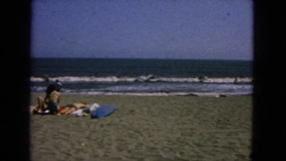 1963 San Francisco beach scene with distant people resting on sand near the surf and blue ocean.