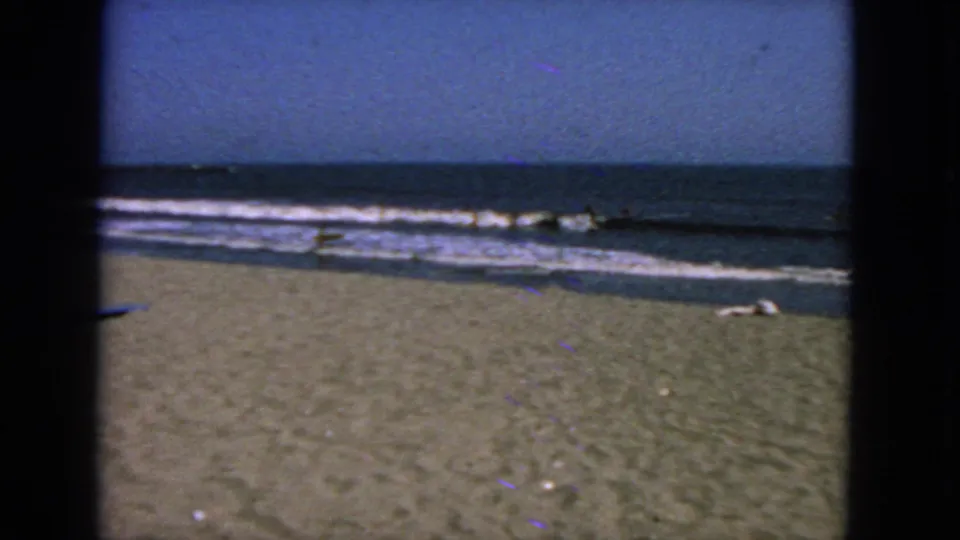 Wide 1963 San Francisco shoreline view with open sand, breaking surf, and small distant figures in the ocean.