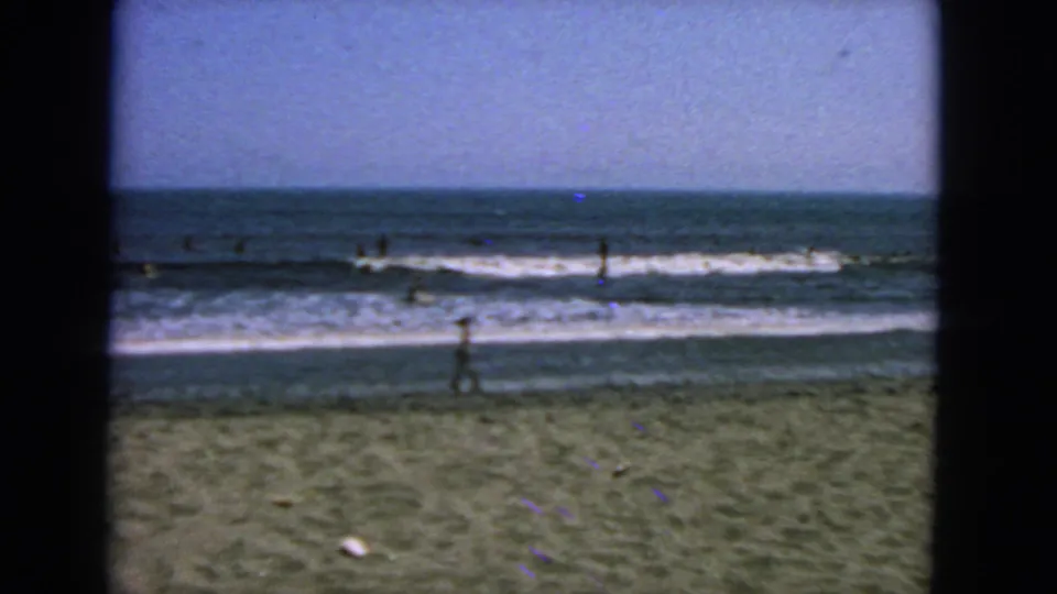 1963 San Francisco beach view with a lone beachgoer in the foreground and distant surfers across the break.
