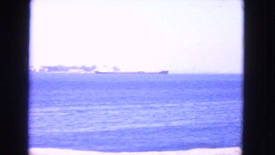 1963 San Francisco 8mm frame showing distant ships across calm blue water, with a pale sky and dark film border.