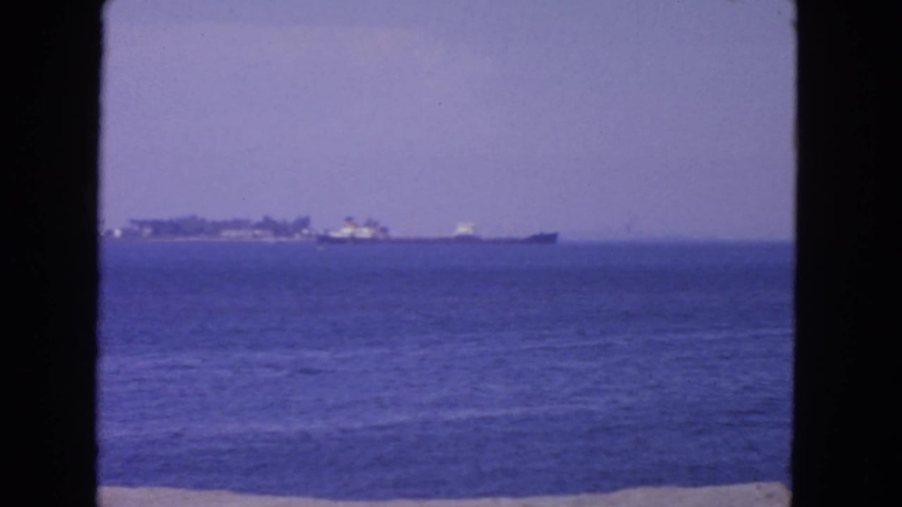 Distant anchored vessels across blue water under a pale sky.