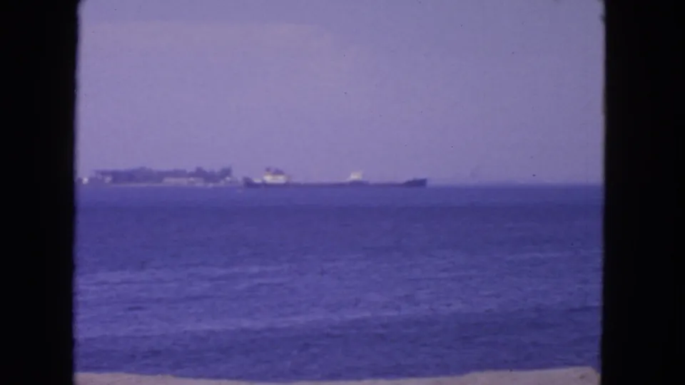 1963 San Francisco home-movie frame with distant ships, calm water, pale sky, and a narrow beach edge at the bottom.