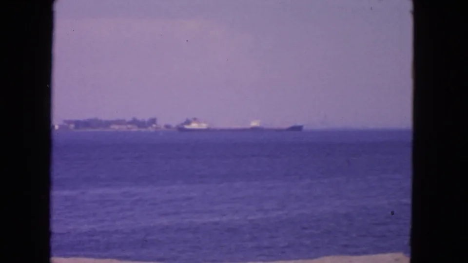 1963 San Francisco Bay frame with a distant large vessel and hazy shoreline seen from across the water.