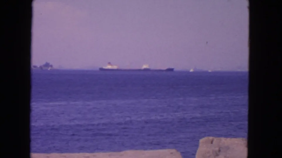 1963 San Francisco Bay home-movie frame showing a distant ship, calm water, and a faint shoreline under haze.