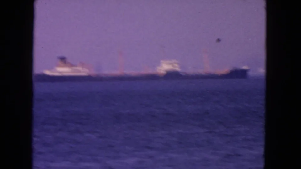 Soft 1963 San Francisco bay frame with a large distant ship, blurred superstructure, blue water, and hazy purple sky.