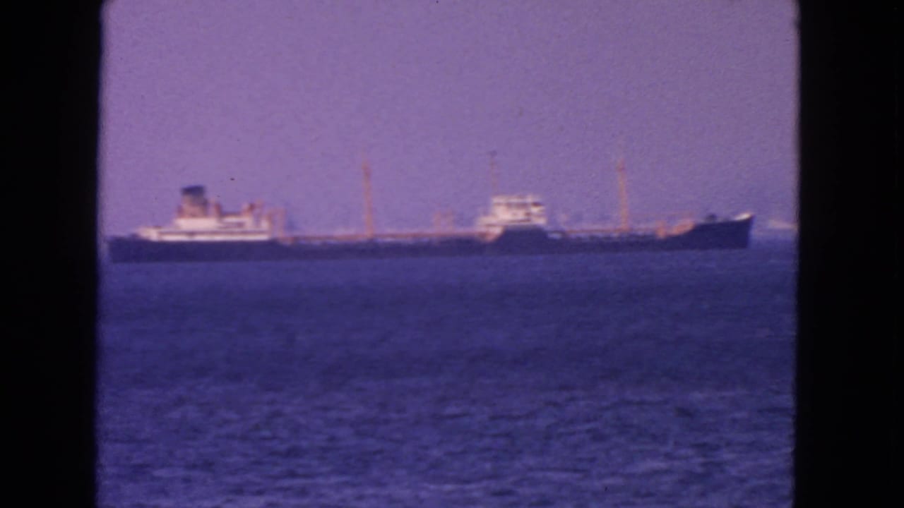 1963 San Francisco Bay home-movie frame showing a distant tanker on calm water beneath a hazy purple sky.