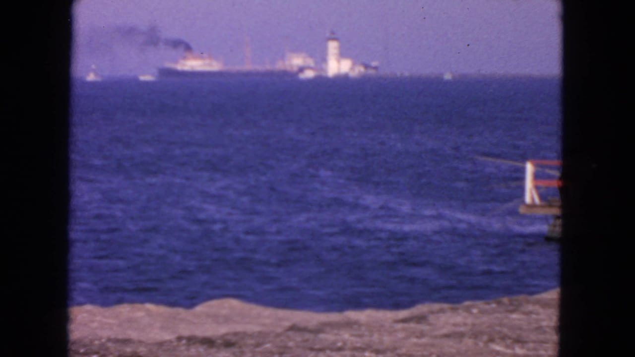 Blue ocean seen through a dark frame with a distant ship and white tower on the horizon.