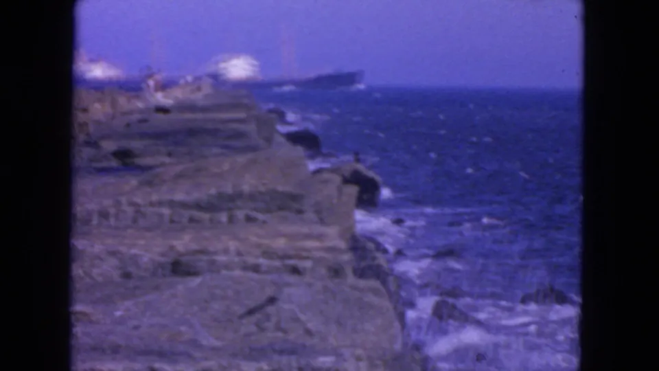 1963 San Francisco shoreline view with surf breaking along rocks and large ships visible offshore.